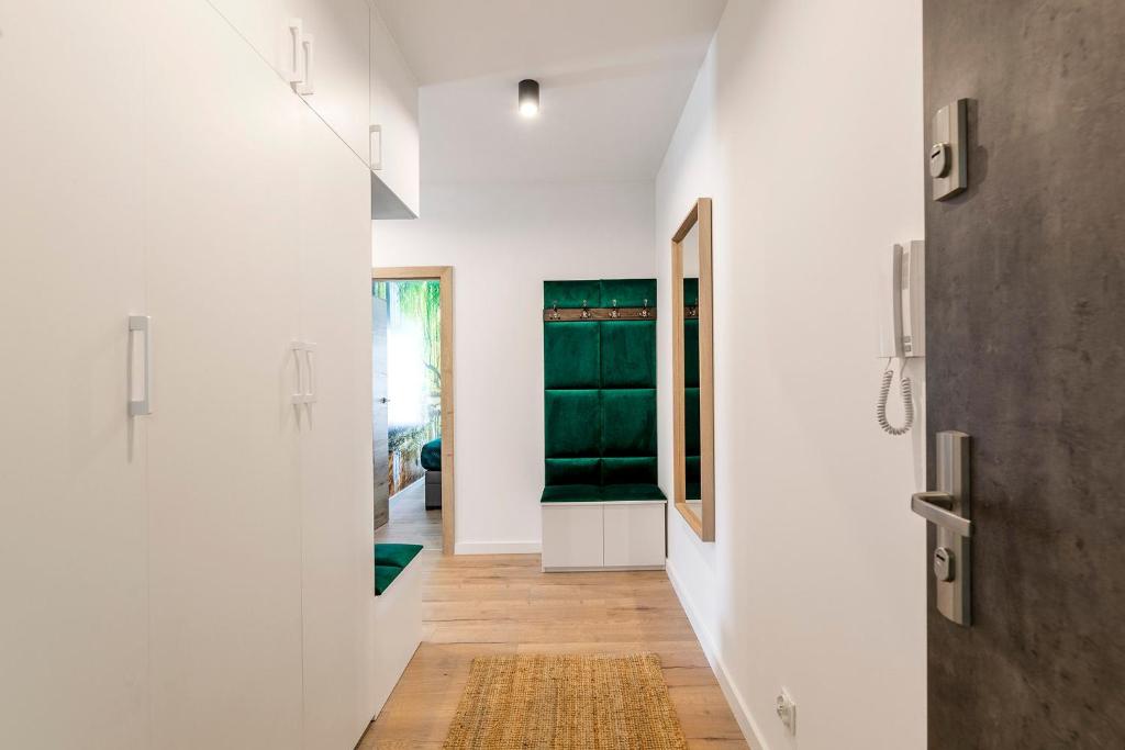 Bright hallway with white cabinetry, emerald upholstered bench, large mirror, and wooden flooring.
