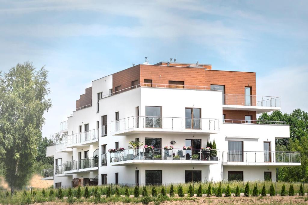 Contemporary white apartment building with glass balconies and planted terraces, grassy foreground and trees.