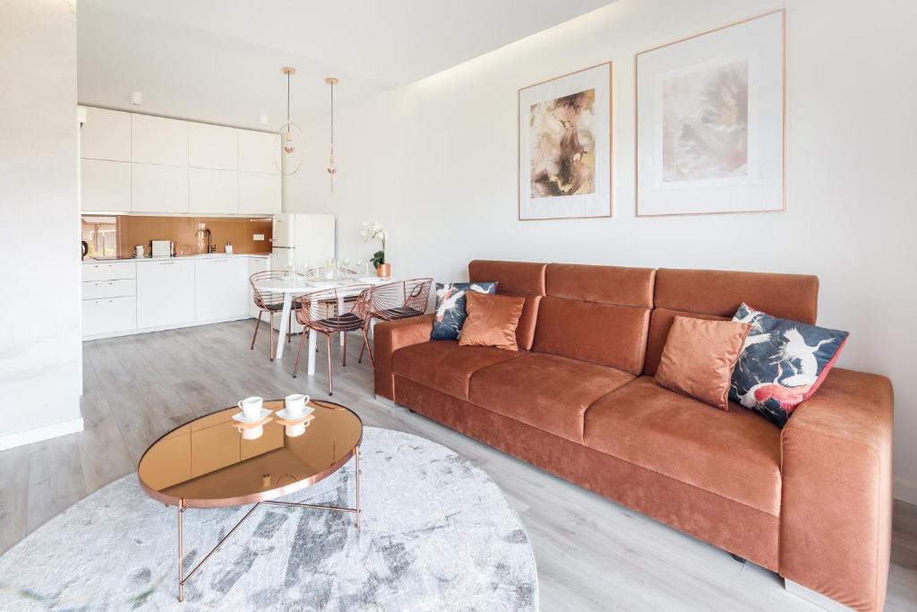 Open-plan living room with rust-colored sofa, copper coffee table, and white kitchen-dining area.