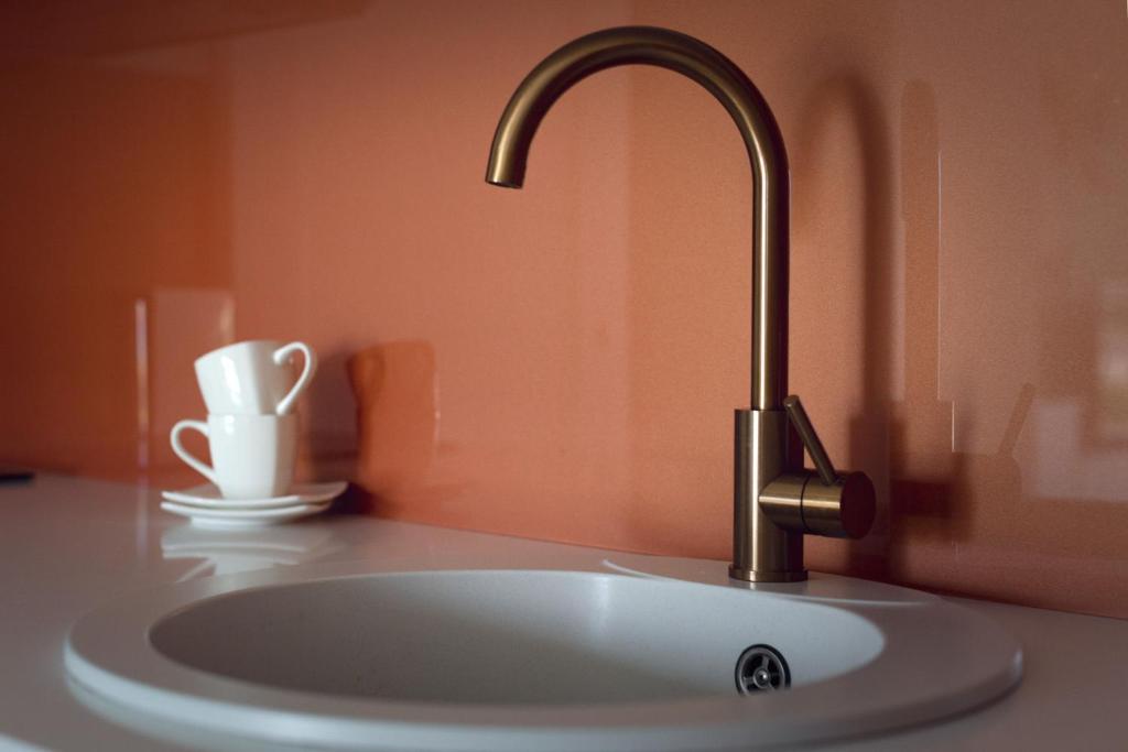 Close-up of bronze faucet and round sink against glossy copper backsplash, stacked white cups.