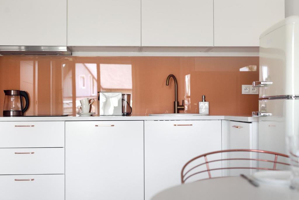 Clean white kitchen cabinets with glossy orange backsplash, chrome faucet, kettle and retro fridge.