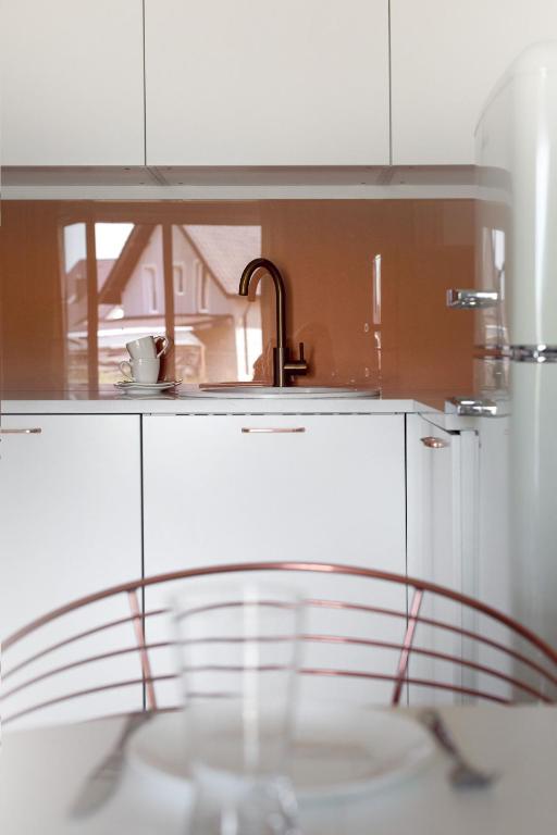 Minimal kitchenette with white cabinets, copper backsplash, single faucet reflected beside stacked cups.