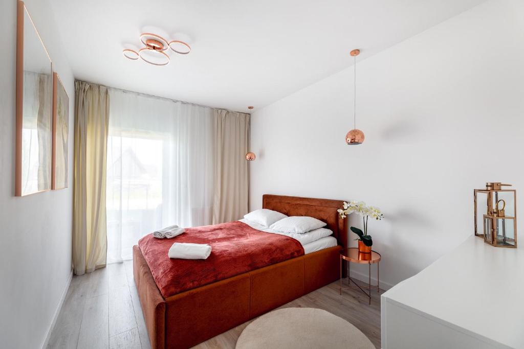 Compact bedroom with rust upholstered bed, folded towels, sheer curtains, warm pendant lighting.