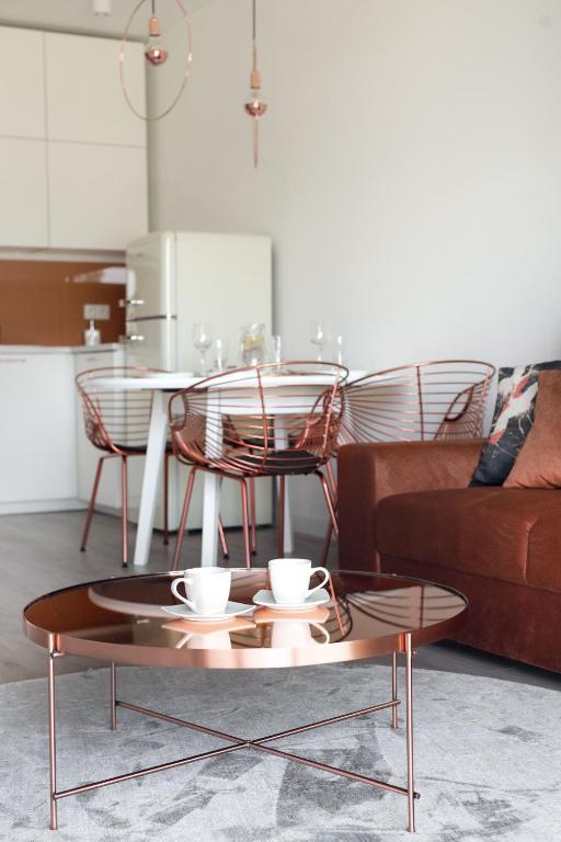 Stylish living area with copper coffee table holding two cups, rust sofa and dining chairs visible.