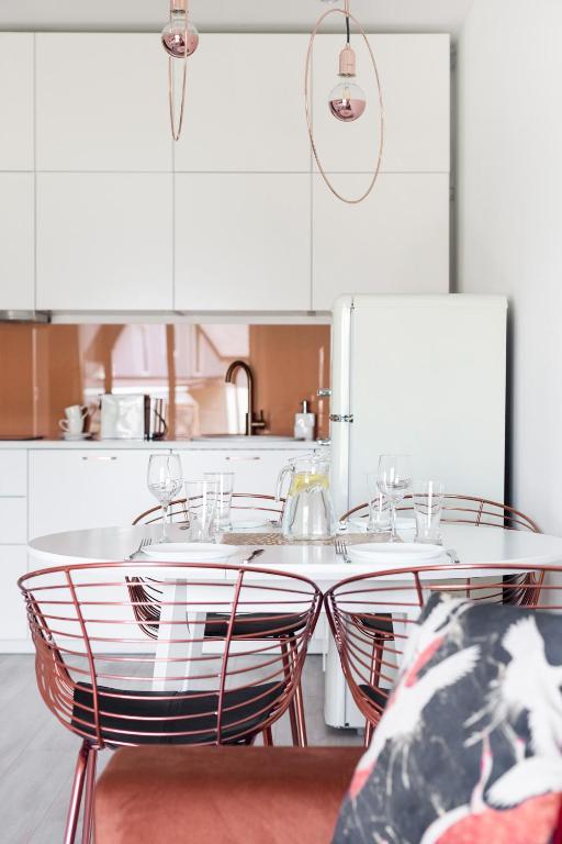 Bright white kitchen and dining area with round table, copper wire chairs, pendant lights, retro refrigerator.