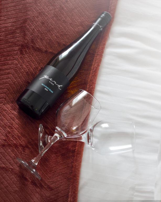 Dark wine bottle and two empty wine glasses resting on burgundy throw across white bed.