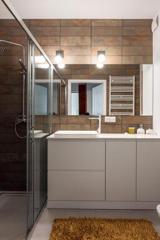 Bathroom vanity with large mirror, sink, and countertop accessories beside glass shower and textured brown tiles.
