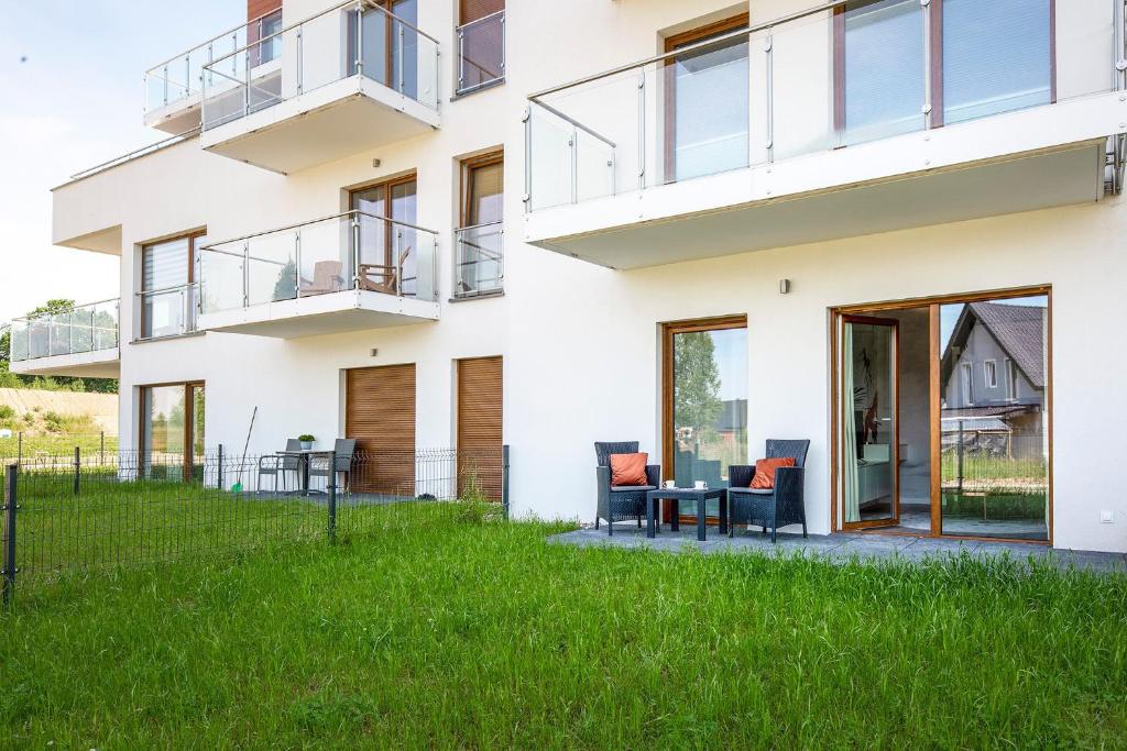 Ground-floor apartment exterior with patio seating, small table, glass balconies above and grassy fenced yard.