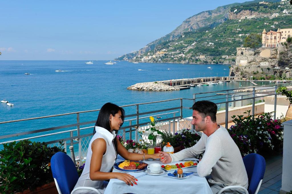 un hombre y una mujer sentados en una mesa con vistas al océano en Hotel Panorama en Maiori