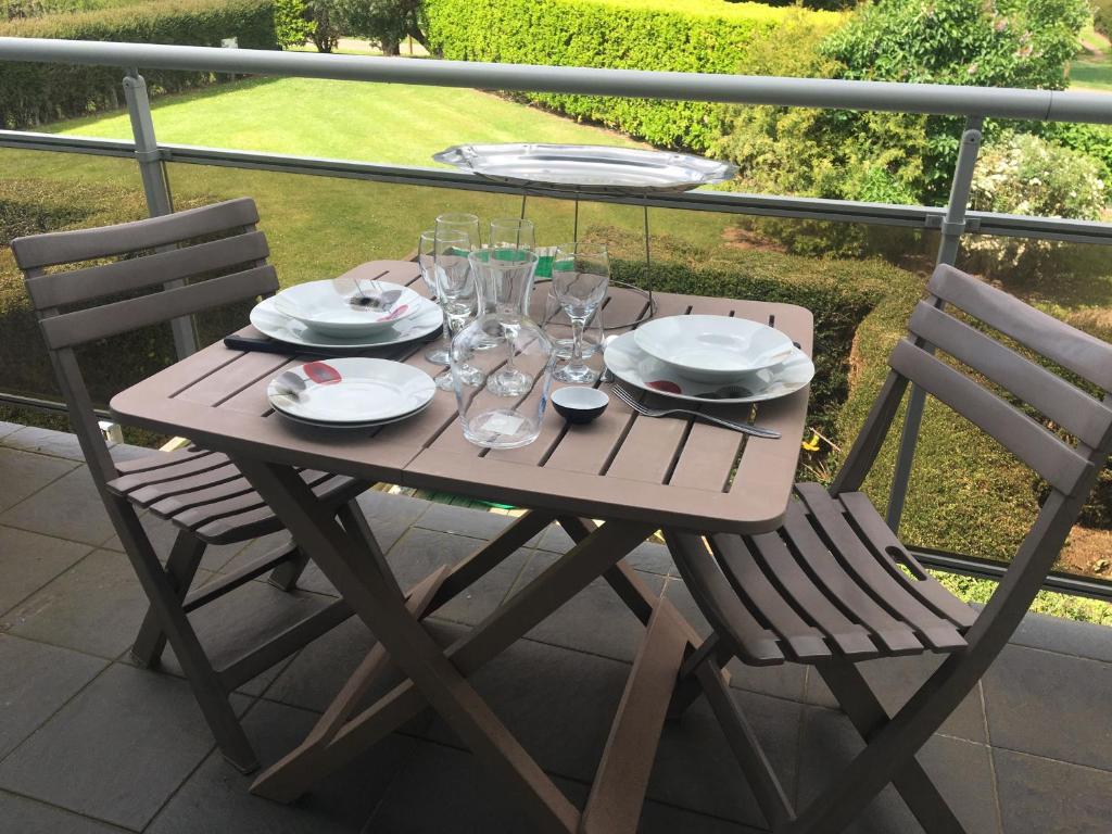 einen Holztisch mit Gläsern und Tellern auf dem Balkon in der Unterkunft Studio Vue sur Jardins - Tout confort Proche Mer in Courseulles-sur-Mer