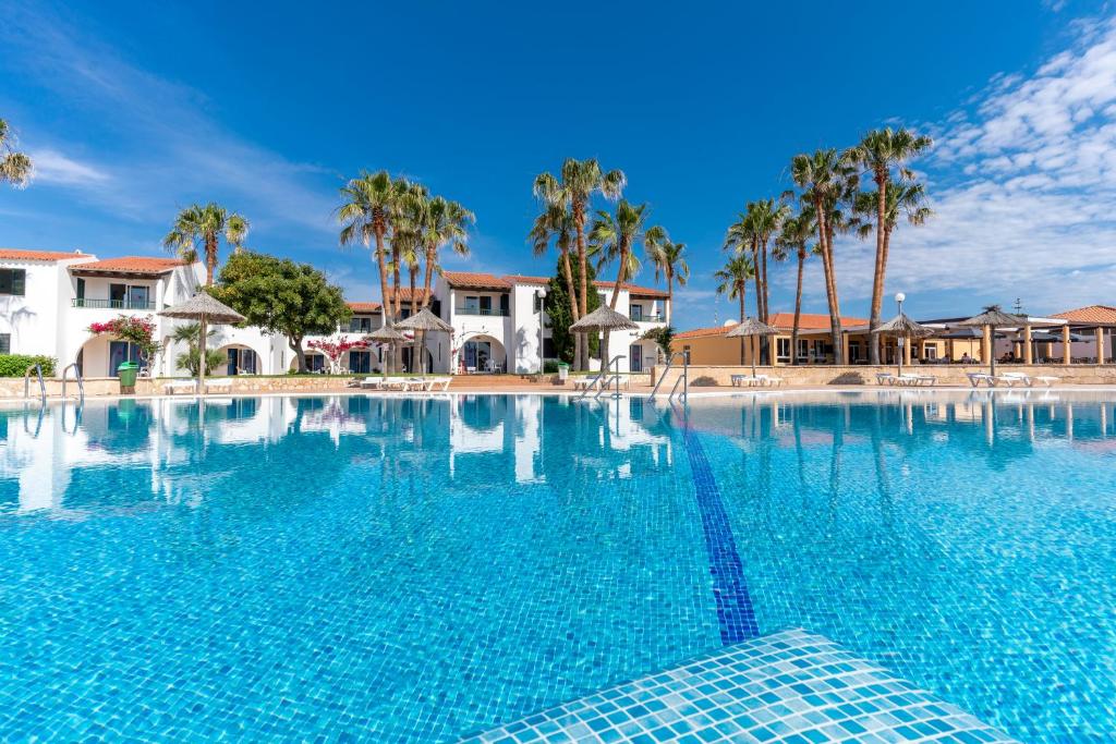 a large swimming pool with palm trees and houses at Apartamentos Vistapicas in Cala en Blanes