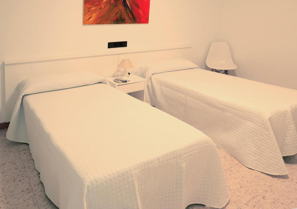 two beds in a hotel room with white sheets at Hostal Lara in Llança