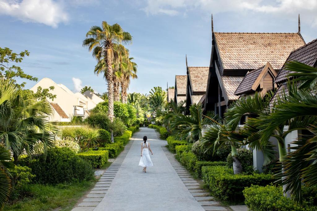 a woman in a white dress walking down a path between houses at Pullman Sanya Yalong Bay Villas & Resort in Sanya