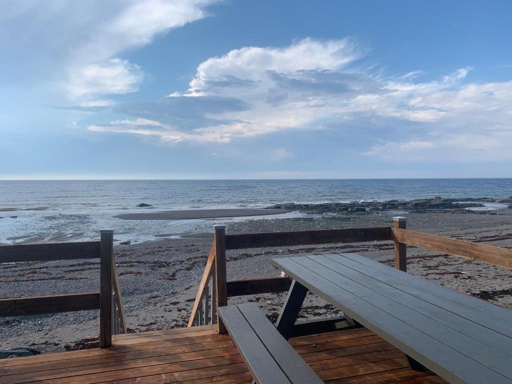 un banco de madera sentado en la playa cerca del océano en Les studios de la mer, en Matane