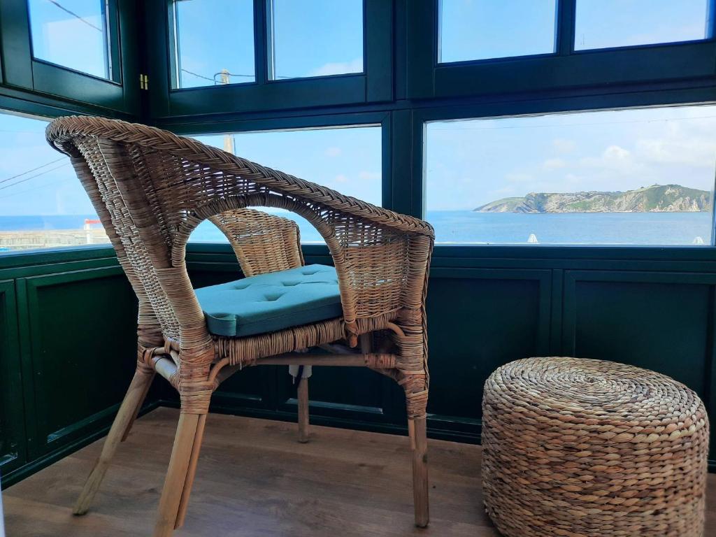 una sedia in vimini in una camera con vista sull'oceano di Apartamentos El Muelle Comillas a Comillas