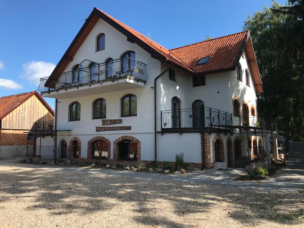 een groot wit gebouw met een rood dak bij Gościniec Twoje Mazury nad jeziorem Śniardwy tuż obok plaży in Nowe Guty