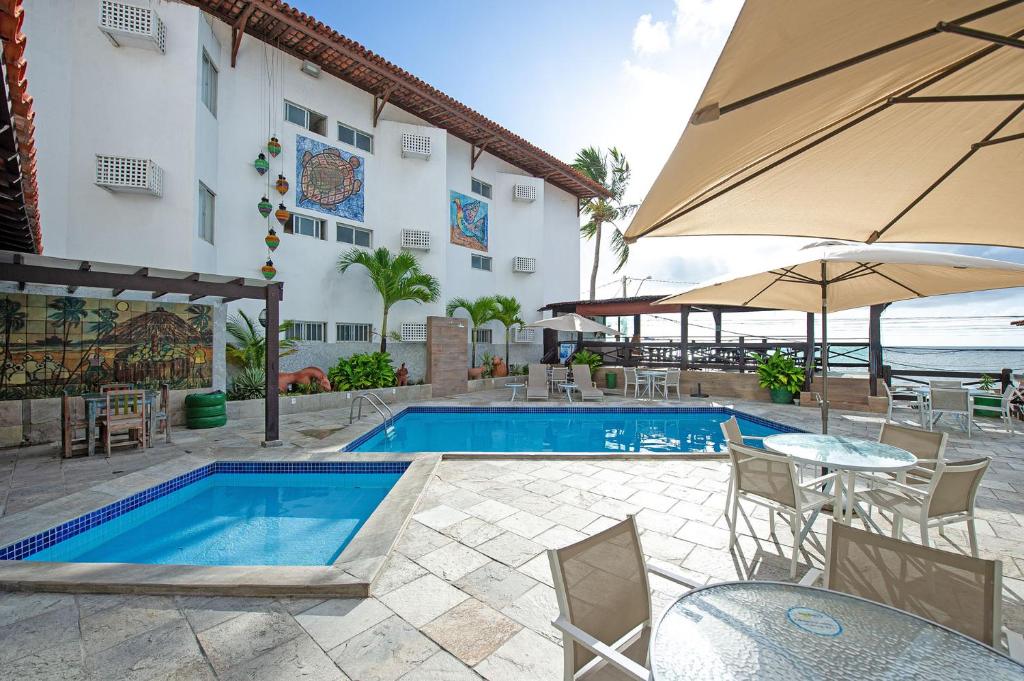 een zwembad met tafels en stoelen en een parasol bij Hotel Costeiro in Olinda