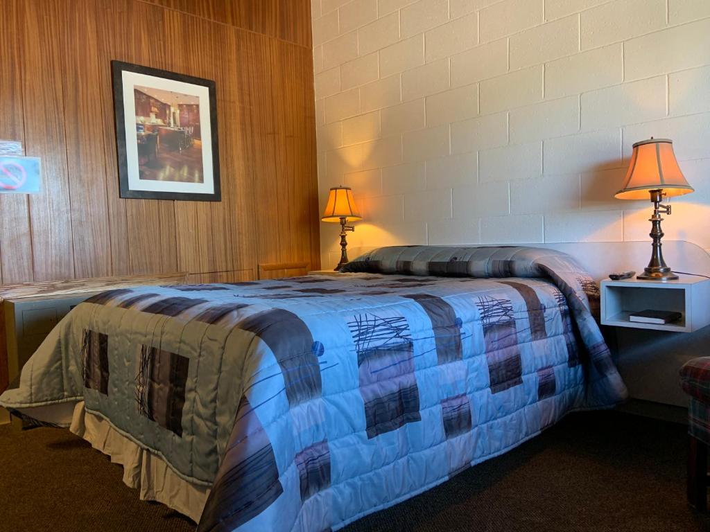 a bedroom with a bed with a blue blanket on it at Ace Crown Motel in Medicine Hat