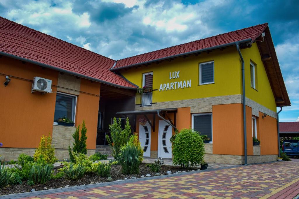 een geel en oranje gebouw met een bord dat lik plantage leest bij LUX Apartman Maroslele in Maroslele