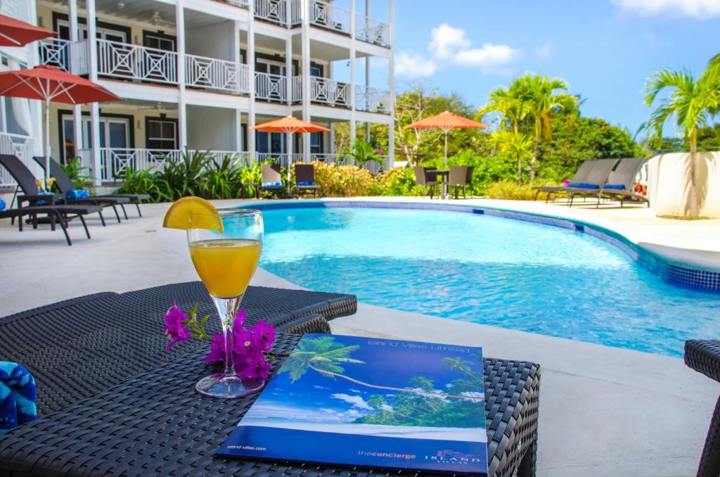 a table with a drink and a book next to a swimming pool at Lantana Resort Barbados by Island Villas in Saint James
