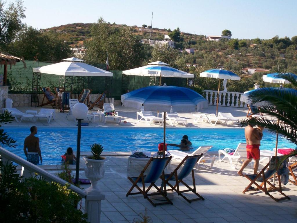 una piscina con sedie e ombrelloni e persone sedute intorno ad essa di Althea Village Residence a Vieste