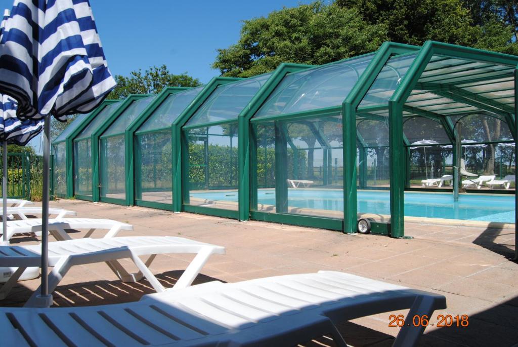 a swimming pool with a green structure with chairs and an umbrella at Village de Gîtes de l'Anse de Moidrey in Moidrey
