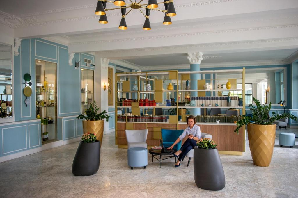 a man sitting on a chair in a room with plants at Hôtel Miléade L'Orangeraie - Menton in Menton