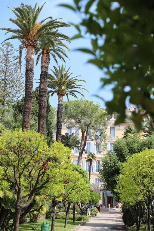 a tree lined street with palm trees and a building at Hôtel Miléade L'Orangeraie - Menton in Menton