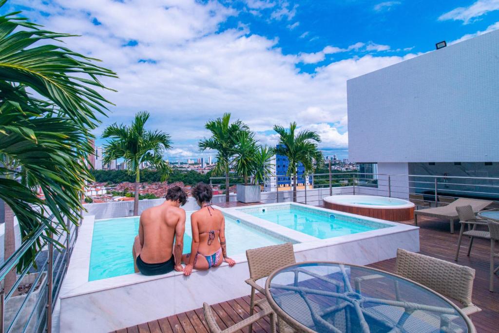 dois homens sentados no telhado de um edifício com piscina em GOLDFLAT - Manaíra by PenareiaTurBr em João Pessoa