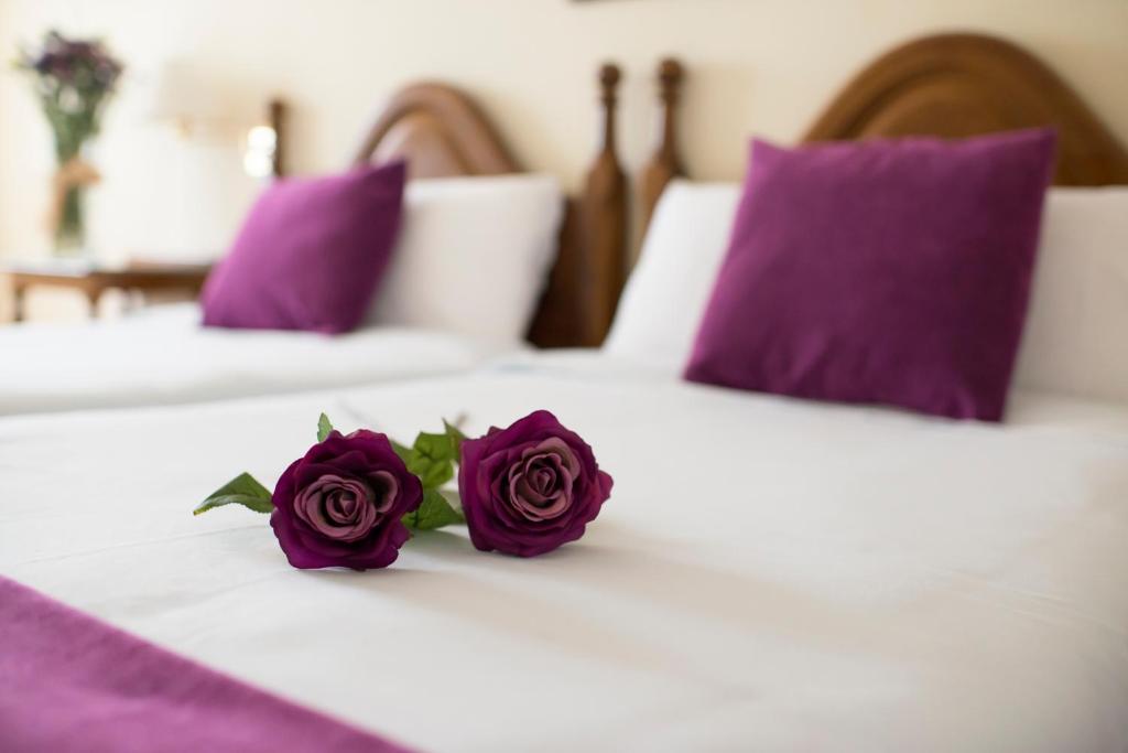 Dos rosas moradas en una cama blanca con almohadas moradas en Villa de Elciego en Elciego