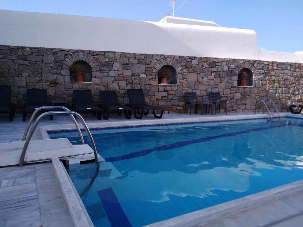 a swimming pool with chairs and a stone wall at Asteri Hotel in Ornos