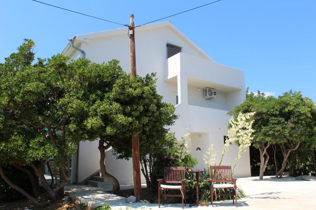 a white house with two chairs and trees at Apartman Boki in Pag