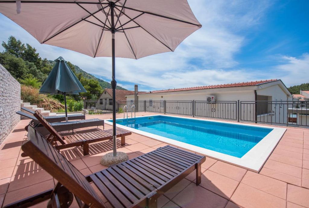 a swimming pool with an umbrella and a bench and a swimming pool at Apartmani Petracie in Drvenik