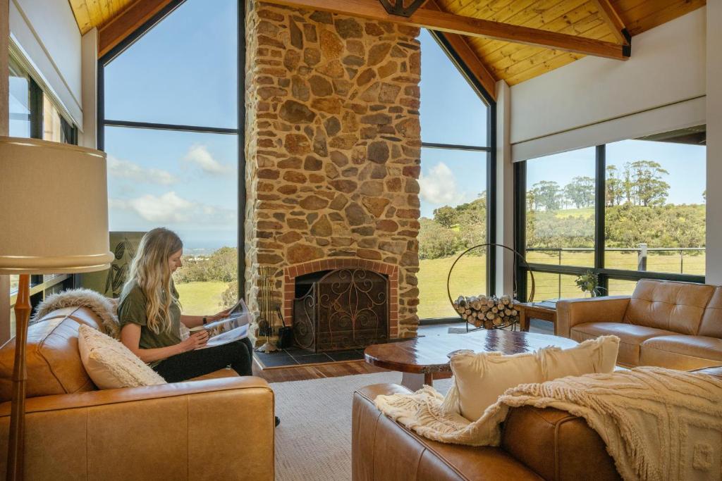 a woman sitting in a living room with a stone fireplace at Old Coach Road Estate in Hindmarsh Valley