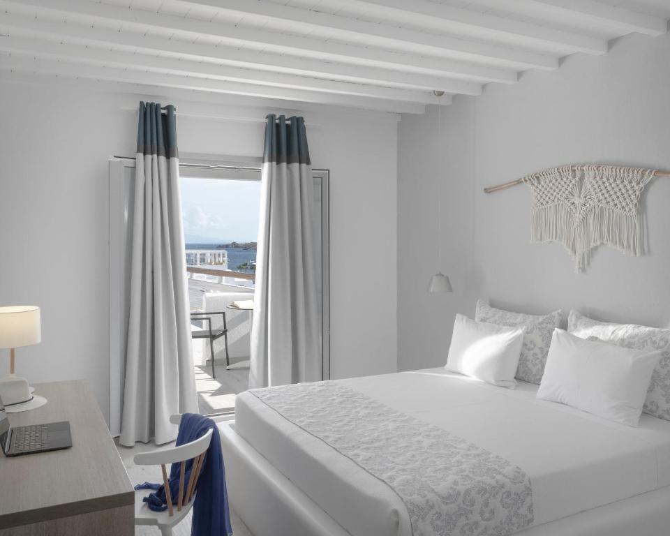 een witte slaapkamer met een bed, een bureau en een raam bij Mykonos Essence Adults Only in Ornos