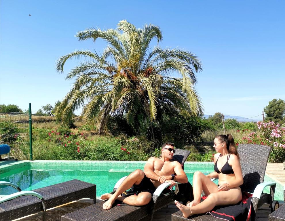 a man and woman sitting in lawn chairs next to a swimming pool at Casona Granado in El Pilar y Provincias