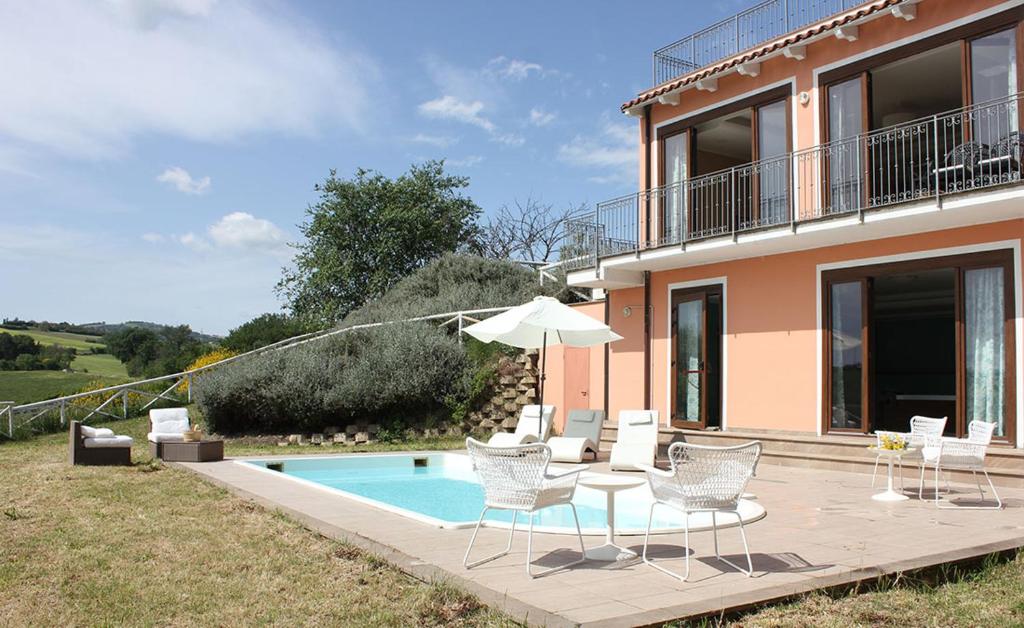 - une terrasse avec des chaises et un parasol à côté d'une maison dans l'établissement Villa Diana - Pesaro mare e cultura - intera struttura con piscina, à Mombaroccio