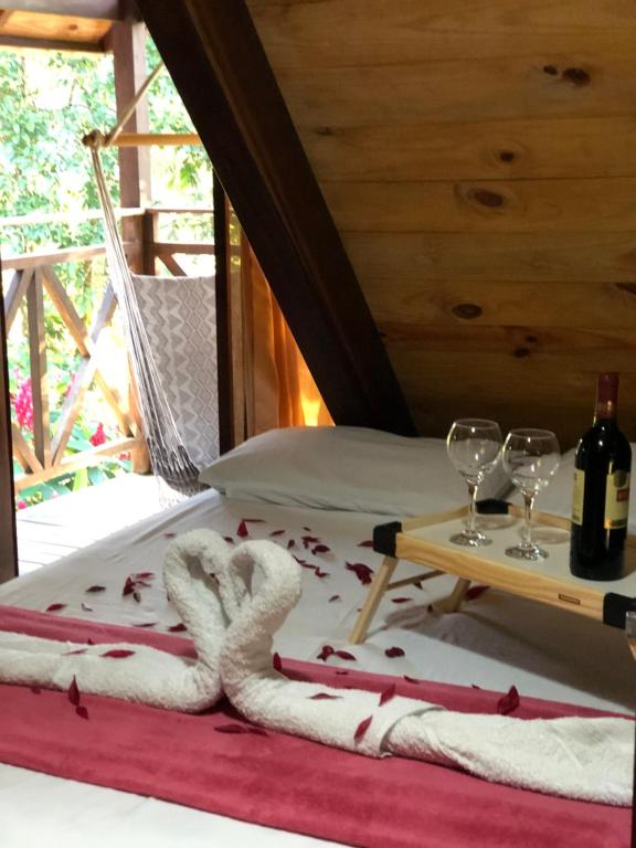 a room with a bed with two wine glasses and towels at Chalé Suíço - Chalés Belo Monte - Sítio Belo Monte in Pacoti