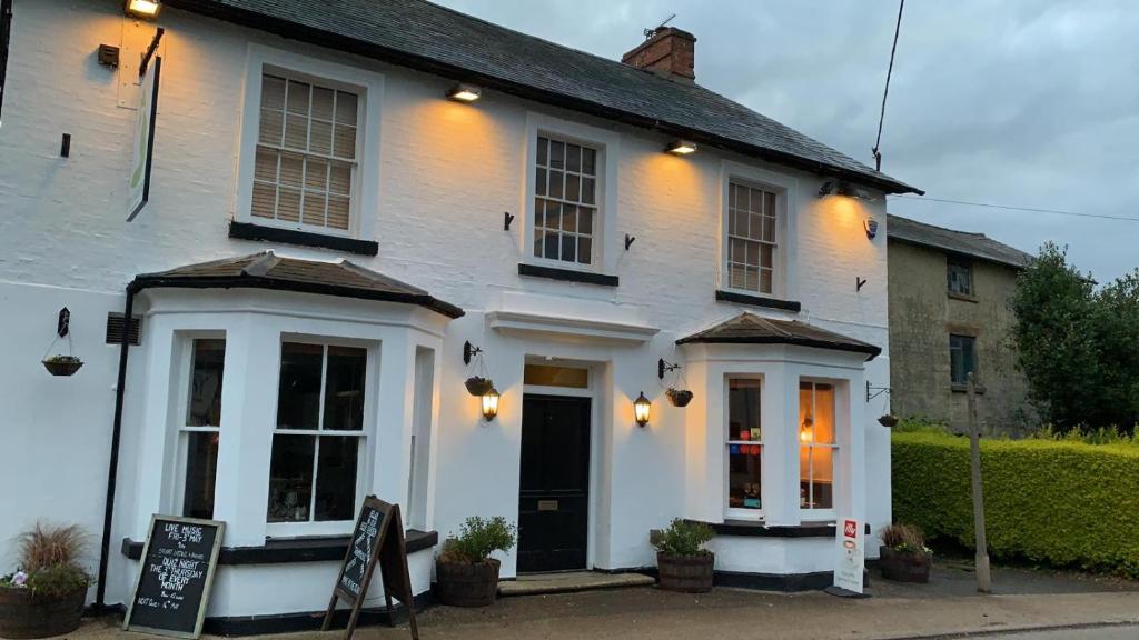 una casa blanca con un cartel delante en The Fox and Hounds en Whittlebury