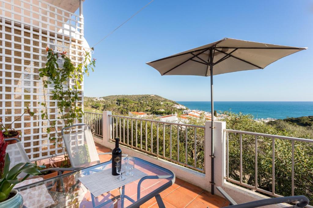 a balcony with a table and an umbrella and the ocean at Apartamento Salema 33 in Salema