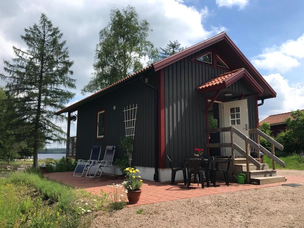 een klein zwart huisje met een terras en stoelen bij Joarsbo, Stuga 2, Gårdsstugan in Kalv