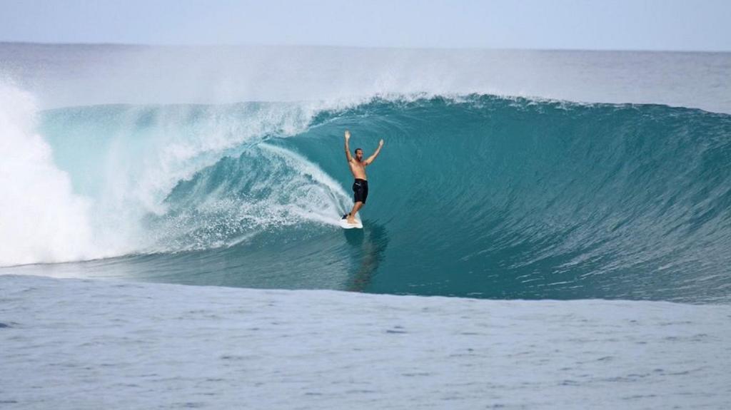 Un uomo che cavalca un'onda su una tavola da surf nell'oceano di Eden Blue a Thulusdhoo