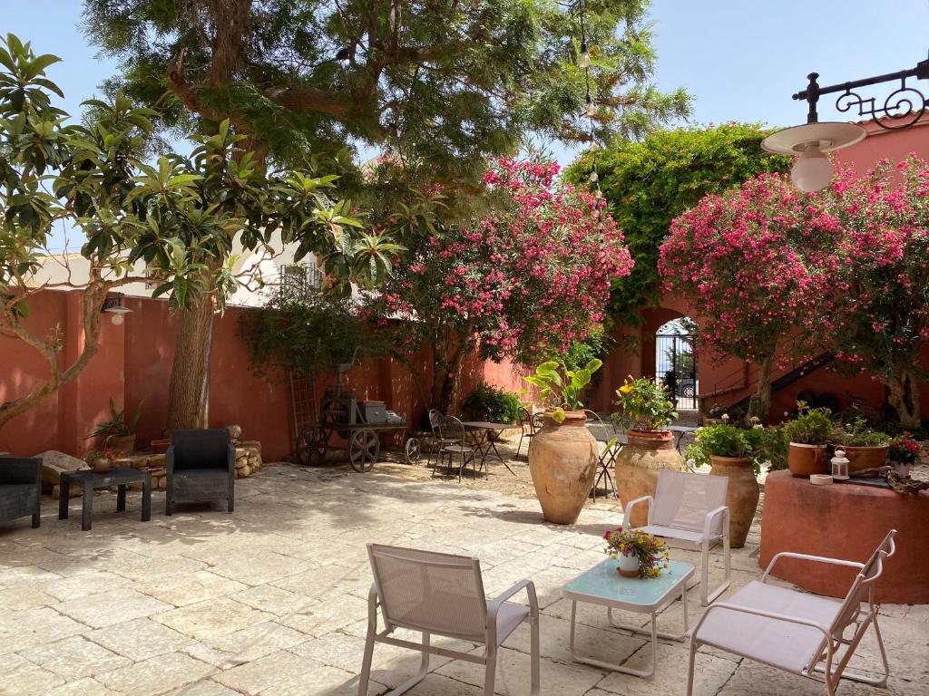 une terrasse avec des chaises, des tables, des arbres et des fleurs dans l'établissement Baglio Buccellato, à Scopello