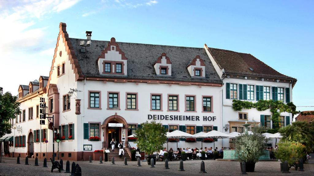 Un grand bâtiment blanc avec des personnes assises à l'extérieur dans l'établissement Deidesheimer Hof, à Deidesheim