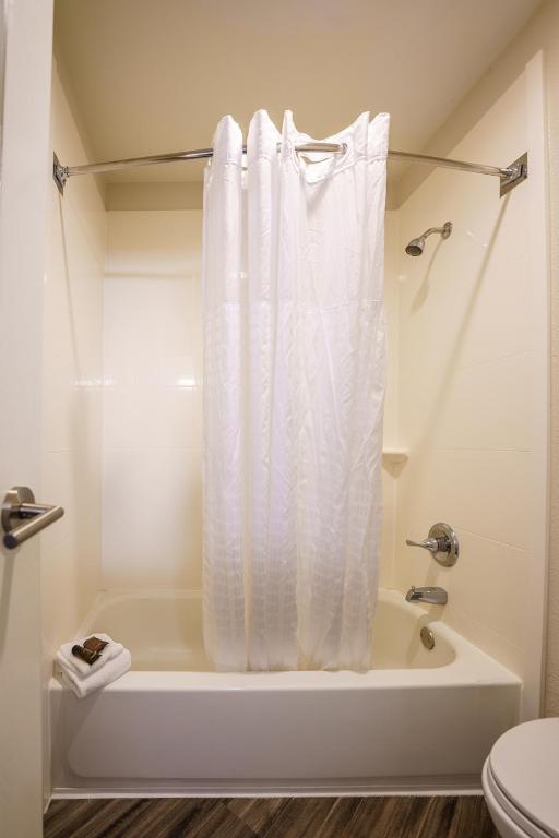 a bathroom with a tub with a white shower curtain at Wingate by Wyndham Brunswick GA I-95 in Brunswick