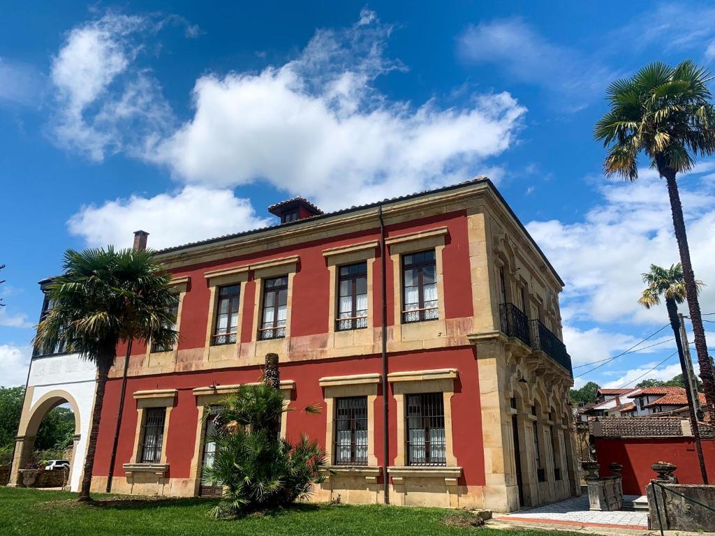 un bâtiment rouge avec des palmiers devant lui dans l'établissement La Venta de Miyares - Casa de Indianos, à Piloña