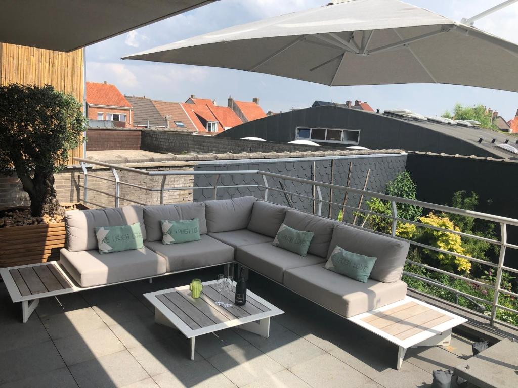 a couch sitting on a balcony with an umbrella at Gezellig appartement op 400m van zee Oostende-Mariakerke Bad in Ostend