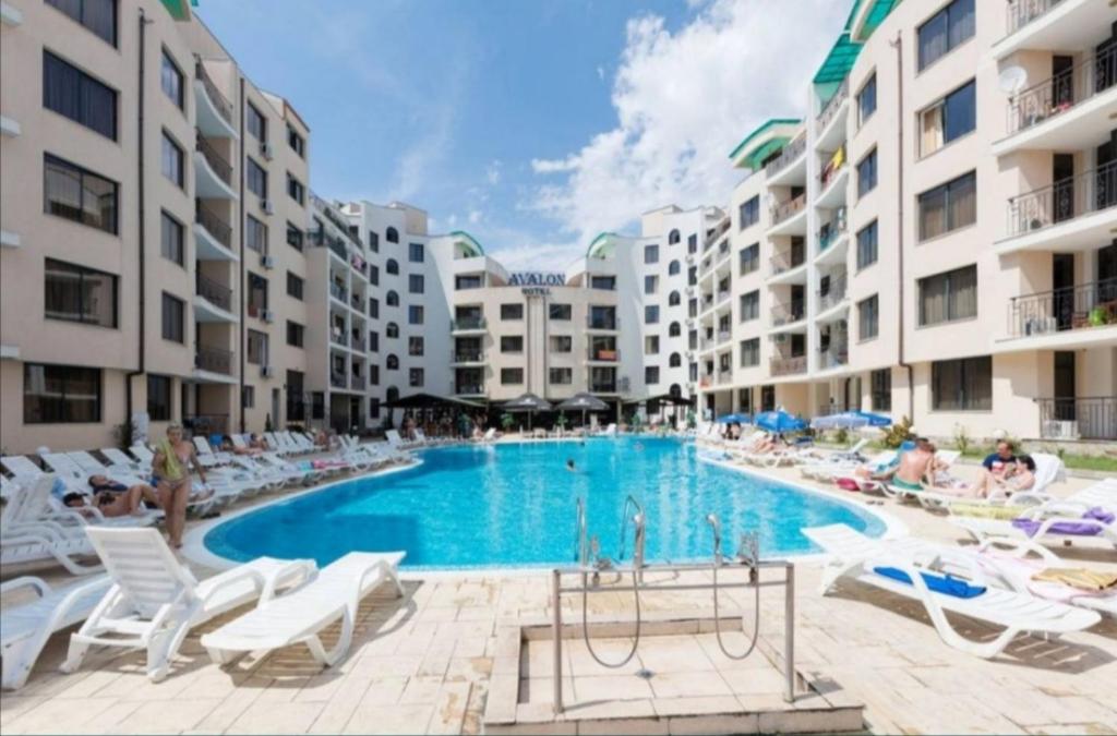 a large swimming pool with white chairs and buildings at Good Vibes apartment Avalon in Sunny Beach