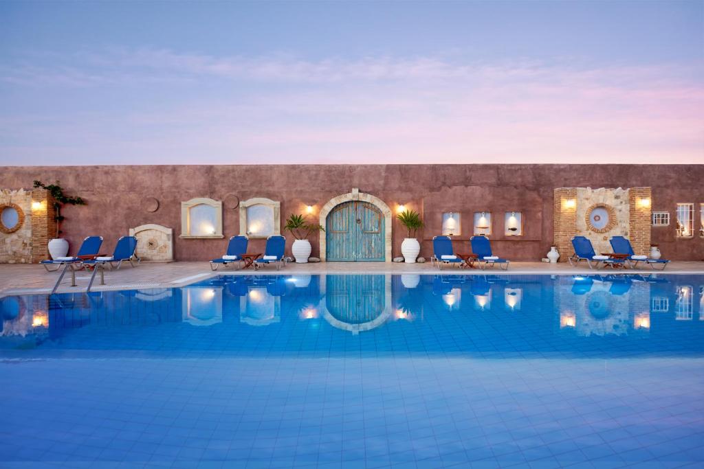 una piscina en un hotel con sillas azules y un edificio en Golden Bay Hotel Apartments, en Malia