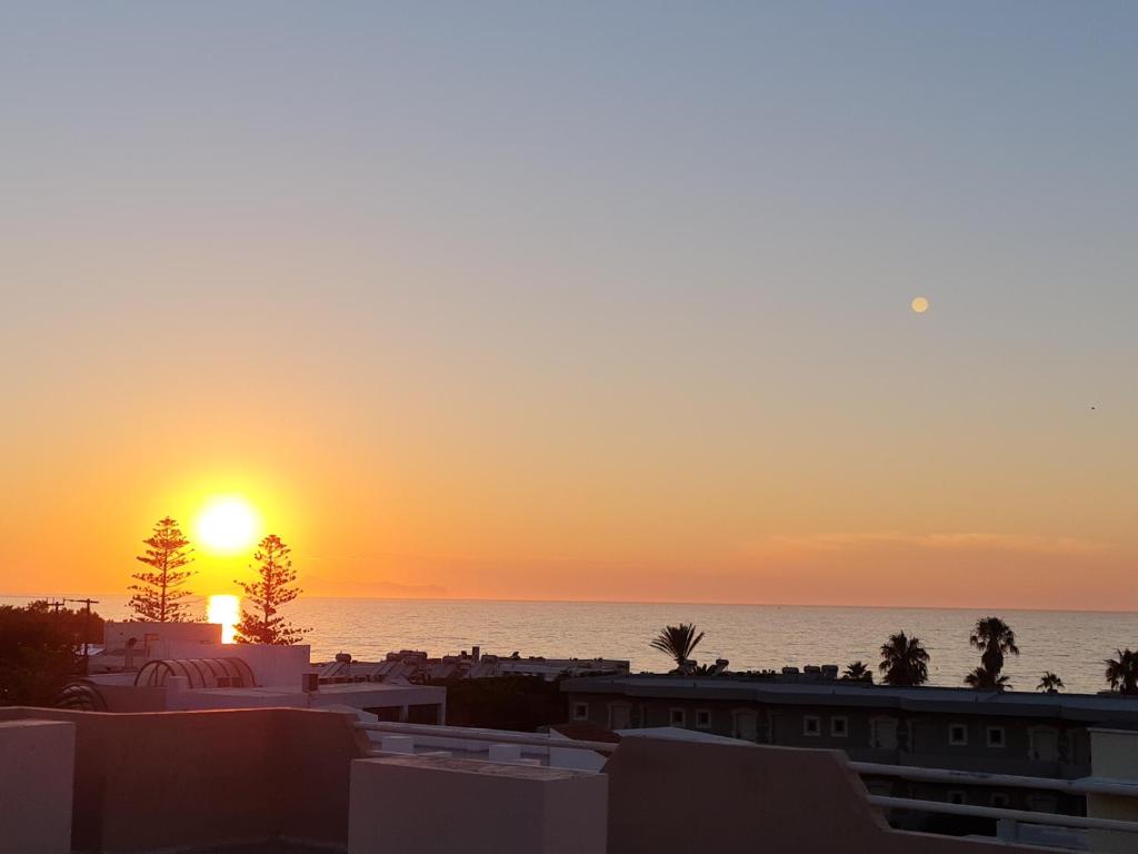 una puesta de sol sobre la playa con edificios y el océano en Dioni Hotel, en Adelianos Kampos